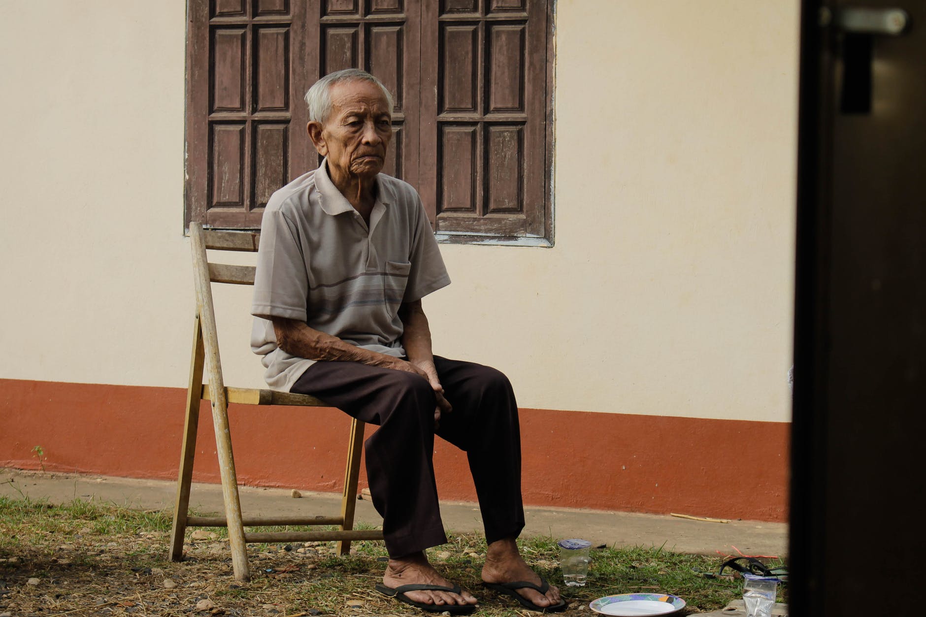 photo of elderly man sitting on wooden chair outside house